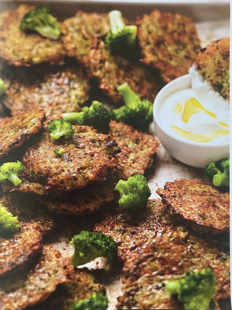 cheese broccoli fritters on a plate, with pieces f cooked broccoli scattered over.